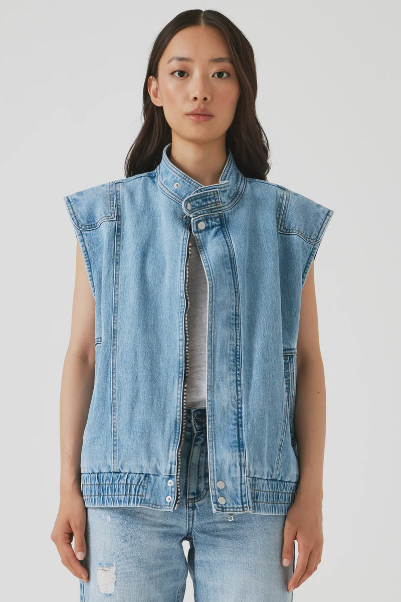 Woman wearing a light blue denim vest over a gray shirt on a white background